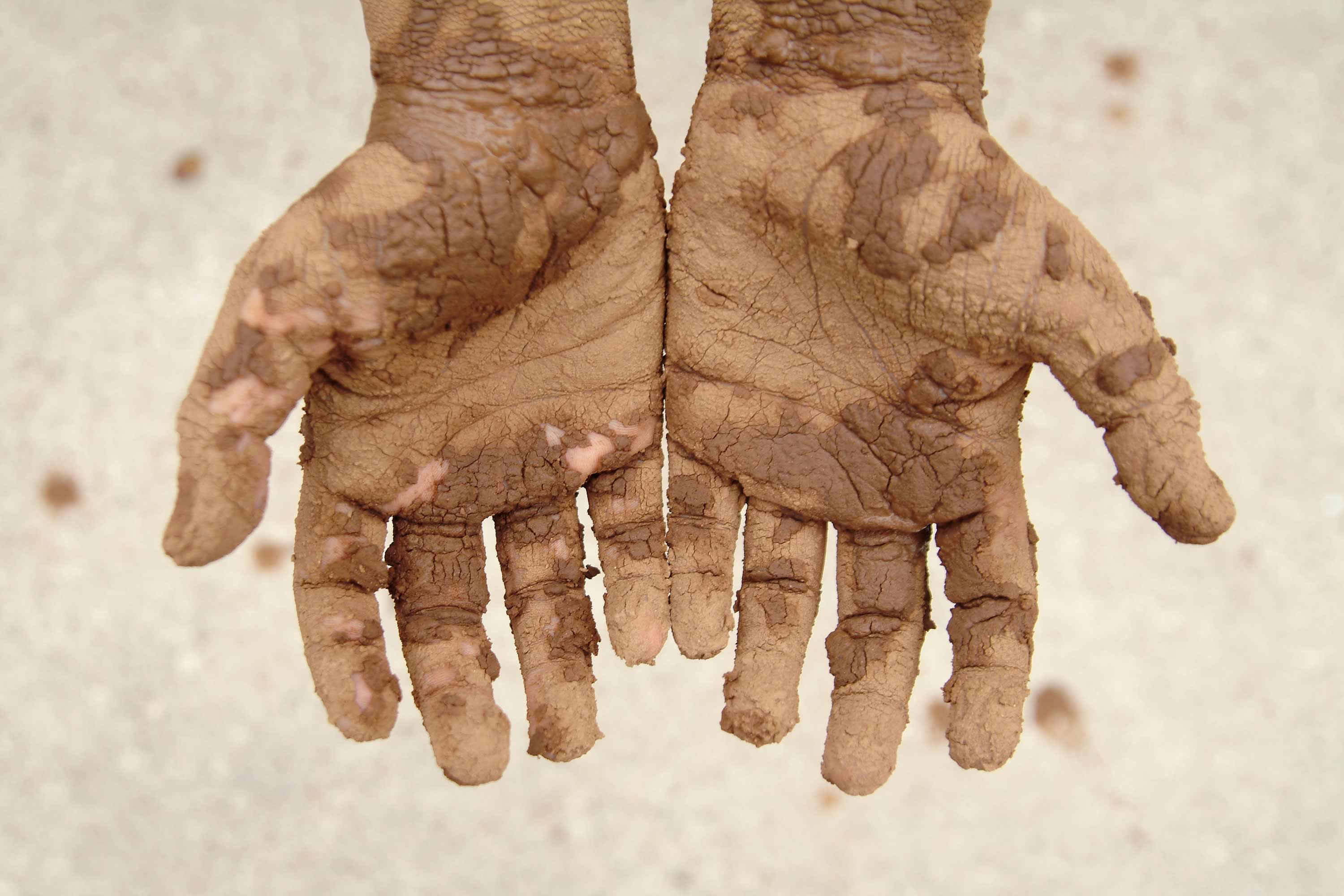 Outstretched hands covered in mud. Photo: iStock / Stephanie Phillips.