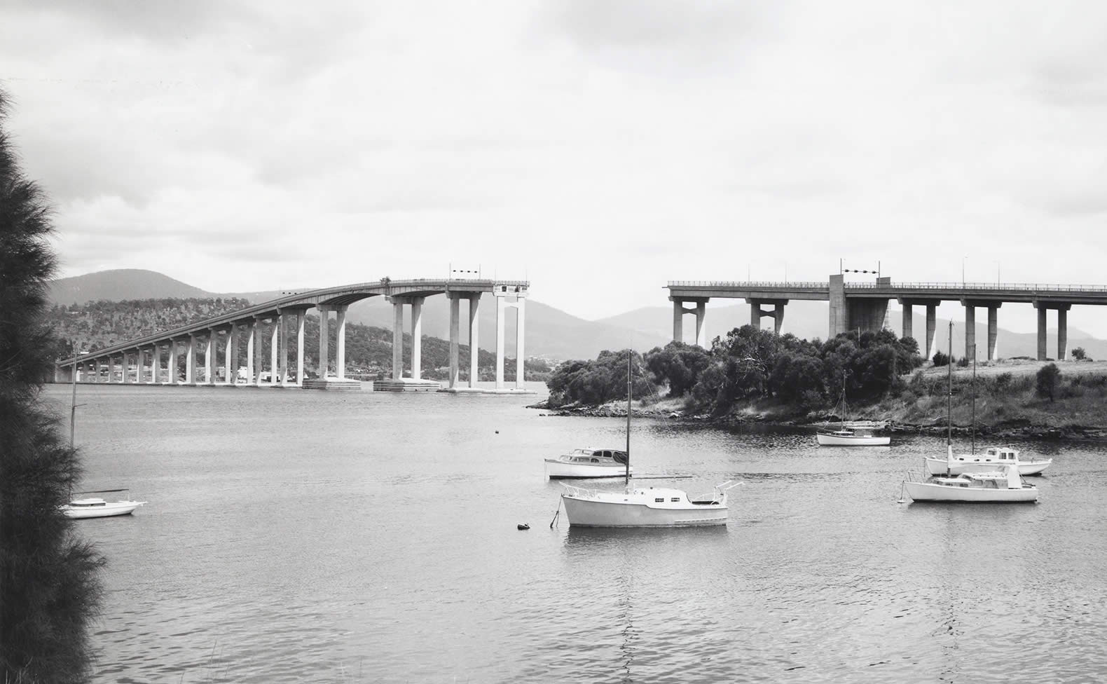 View of the Tasman Bridge from Kalatie Road Montagu Bay looking toward the Powder Jetty over Cuthbertson’s Boat shed (1975). Photo: Tasmanian Archive and Heritage Office.